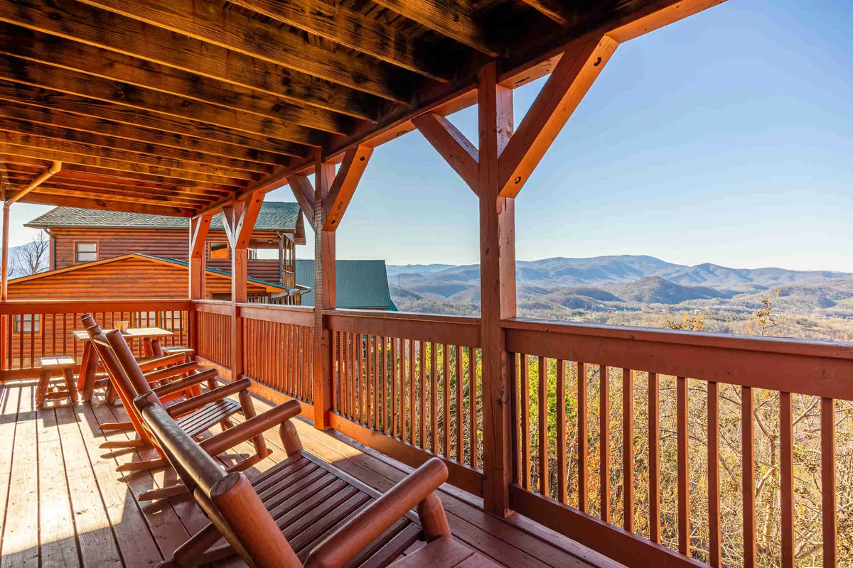 This image shows two classic wooden rocking chairs set on a deck, overlooking a breathtaking mountain vista. The morning light casts a soft glow, highlighting the tranquility of the scene. The wooden railing and untouched natural landscape create a sense of seclusion and intimacy, perfect for couples to share a peaceful sunrise together.