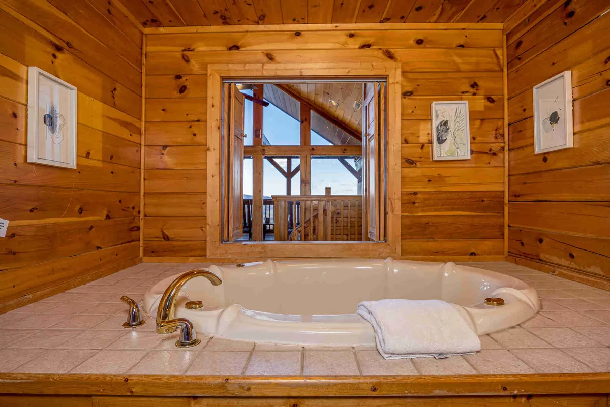 A tranquil bathroom with a jacuzzi tub positioned by a large window, surrounded by wooden walls and enhanced with framed artwork. The space offers not just luxury, but scenic views and an atmosphere perfect for relaxation or romantic escapes.