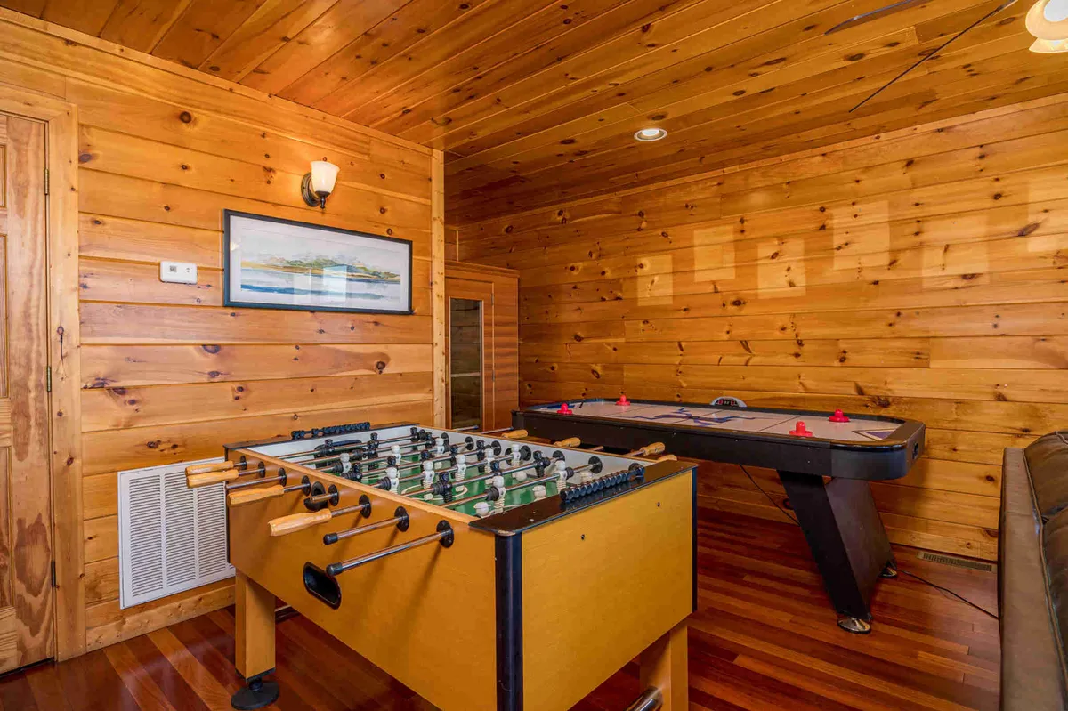 An energetic game space equipped with both a foosball and air hockey table, framed by wood-paneled walls and lively artwork. A couch in the background provides a spot to relax between games, underscoring the room’s versatility.