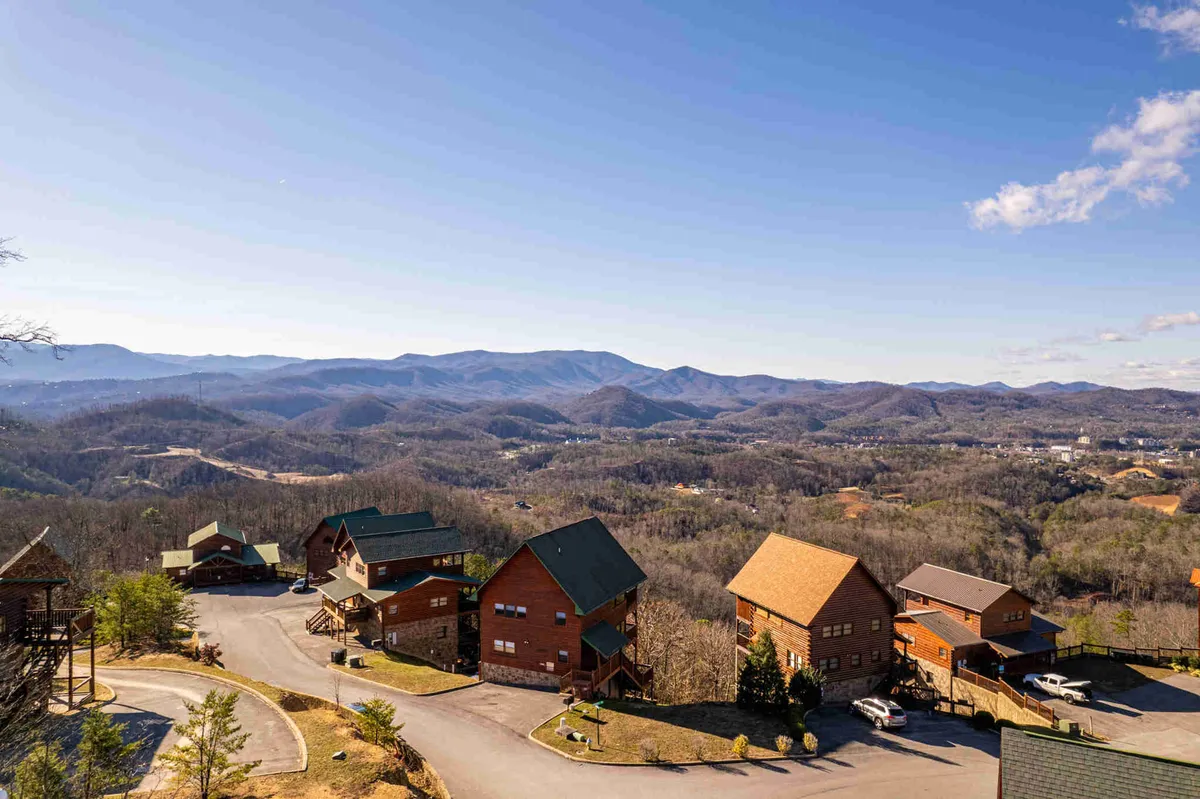 A peaceful exterior shot featuring log cabins nestled along a winding road surrounded by rolling mountains. The scene is tranquil, with plenty of greenery and a sense of seclusion, emphasizing the retreat aspect after a day outdoors.