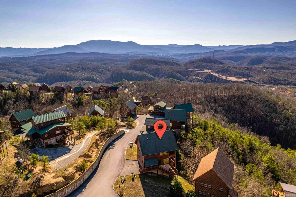 This image shows a picturesque exterior view of a cozy cabin set against a backdrop of Smoky Mountain ranges. The cabin's inviting architecture is framed by nature, with a winding road leading towards it, emphasizing connection to outdoor adventures. The porch and visible windows suggest welcoming spaces for families to gather and relax after a day of exploration.