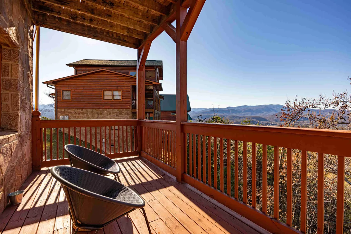 Two black chairs are placed on a wooden deck, facing a stunning mountain panorama. The scene is serene and intimate, inviting couples to relax and savor the view together. The setup suggests an ideal spot for enjoying a glass of wine or soaking in the peaceful ambiance as the sun sets.