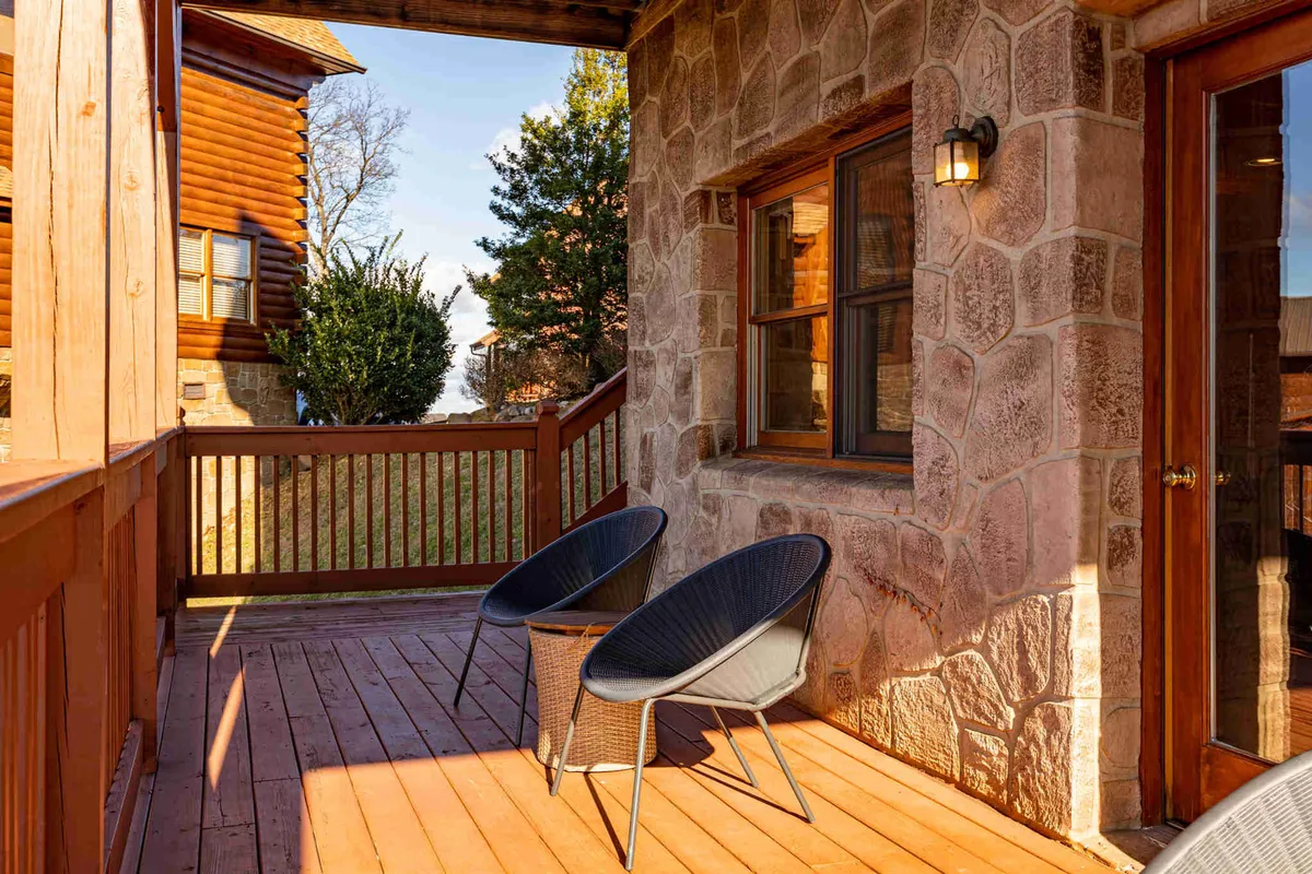 A peaceful wooden deck featuring a stone wall, two comfortable chairs overlooking a scenic natural landscape. The deck is bathed in calm daylight, ideal for morning coffee or quiet evening relaxation.