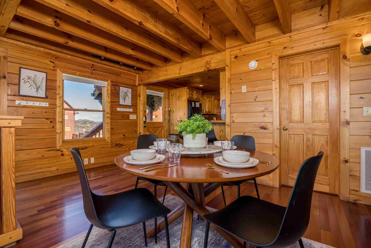 A wooden dining table surrounded by black chairs sits prominently in a warmly lit dining area. Decorative touches like a plant centerpiece and framed botanical artwork add to the inviting, communal feel, suggesting memorable family meals and celebrations.