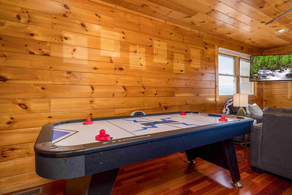 An inviting interior scene with a dedicated entertainment area featuring an air hockey table, wood-paneled walls, a TV, and cozy seating. The space exudes a playful and welcoming atmosphere, ideal for game nights and bonding after a day of adventure.