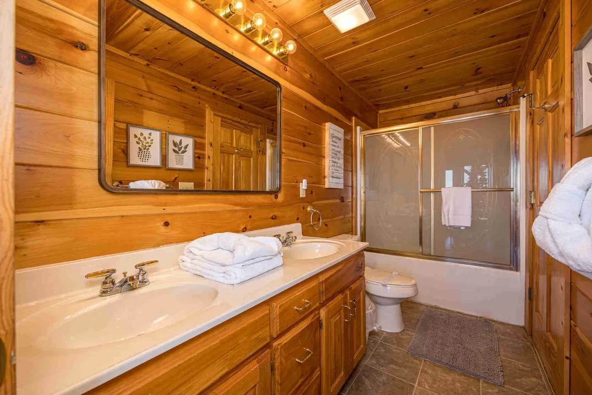 A spa-inspired ensuite bathroom with double vanity sinks, a large mirror, wooden paneling, and a glass shower enclosure. The space feels welcoming, modern, and ideal for unwinding after a day of adventure.
